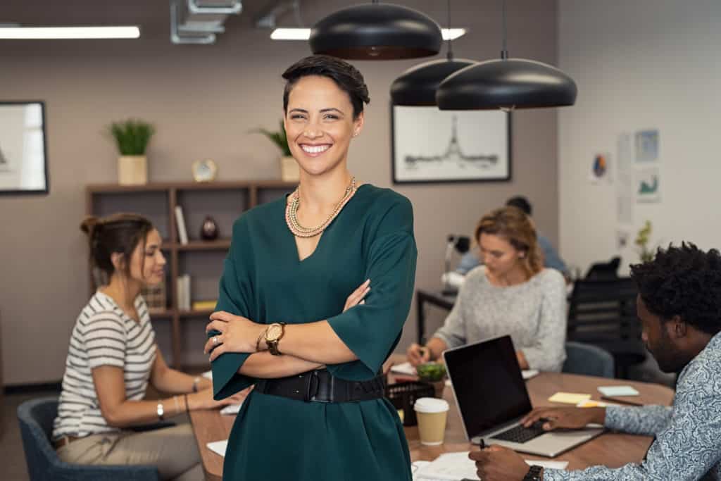 Portrait of successful business woman standing with her colleagues working in background at office.
