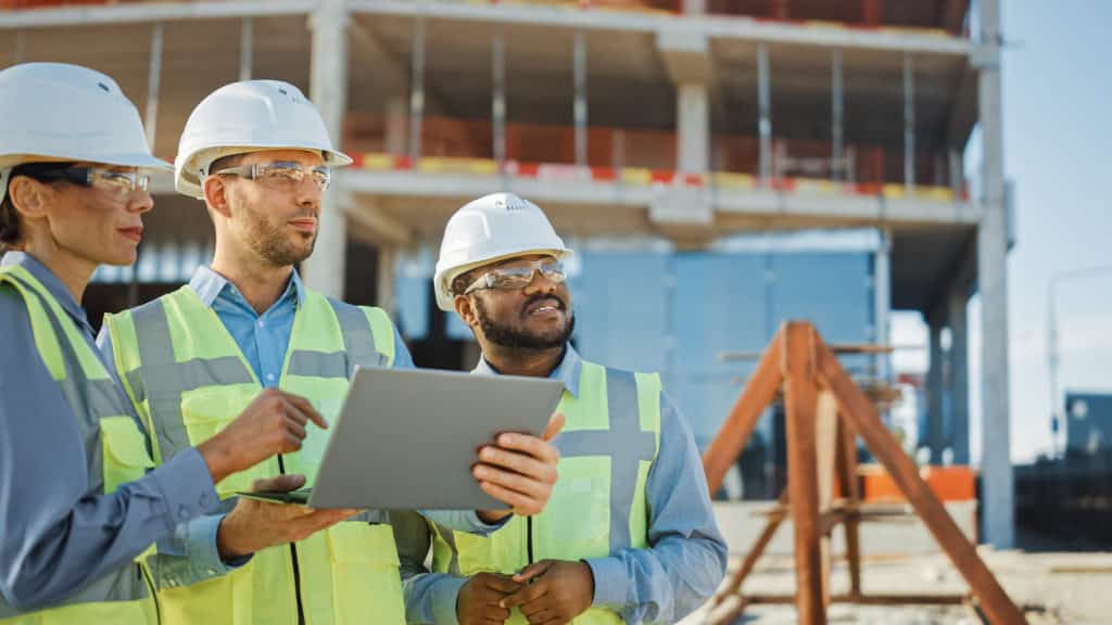 Diverse Team of Specialists Use Laptop while surveying a Construction Site