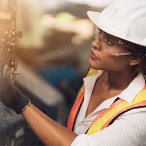 Woman wearing a hardhat and safety glasses, inspecting machinery
